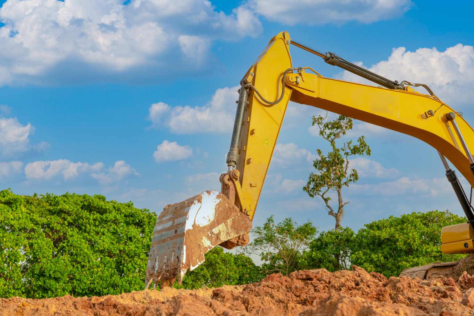 Yellow excavator moving dirt in an open, grassy field