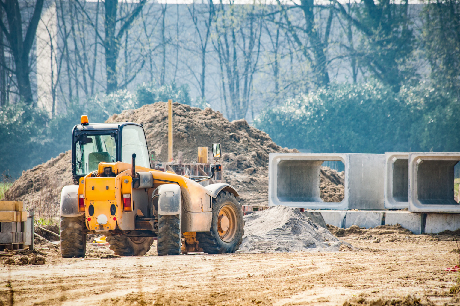 White backhoe loader parked next to concrete pipes.